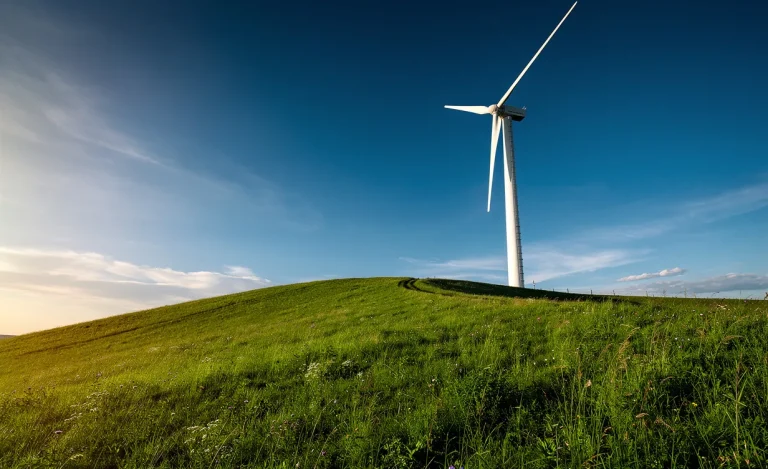Une éolienne moderne se dresse sur une colline verdoyante sous un ciel bleu dégagé, baignée de la lumière du soleil.