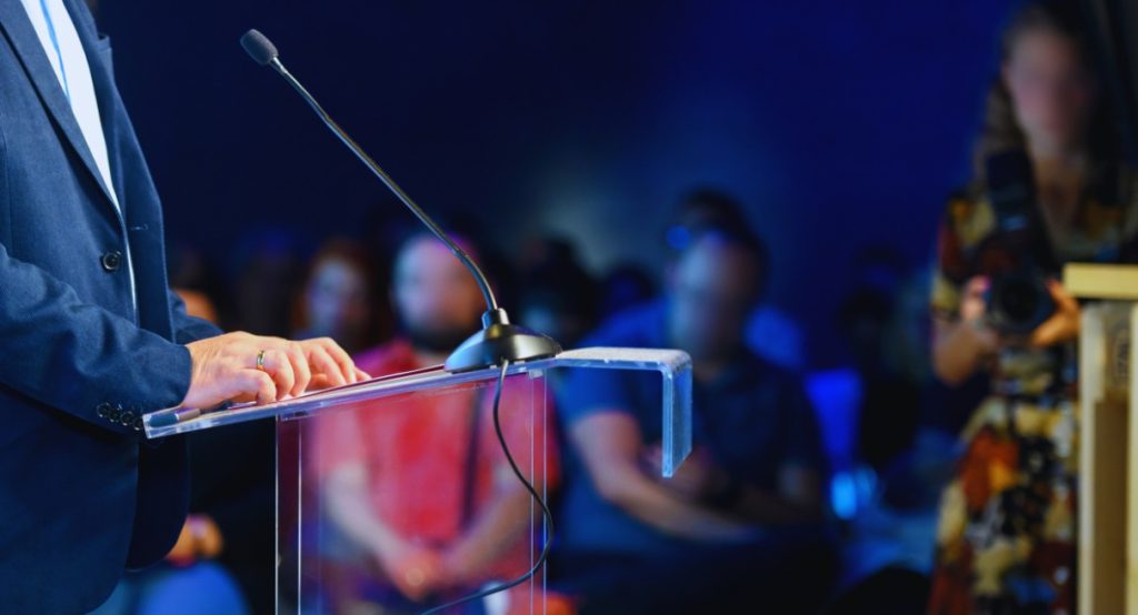 Orateur à une tribune avec microphone devant un public lors d'un débat politique