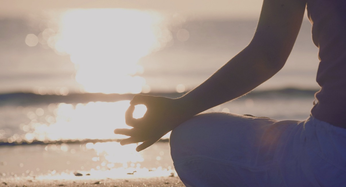 Personne en méditation sur la plage au coucher du soleil, évoquant la signification spirituelle de l'heure miroir 19h19 au travail