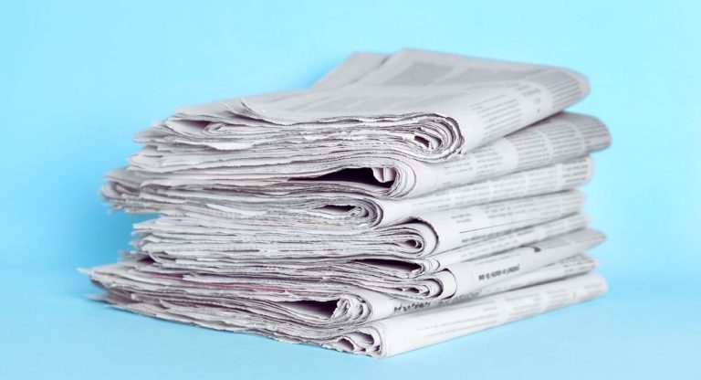 Pile de journaux plies posee sur un fond bleu clair