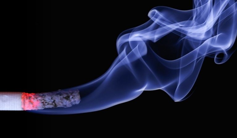 Cigarette incandescente dégageant des volutes de fumée bleutée sur fond noir