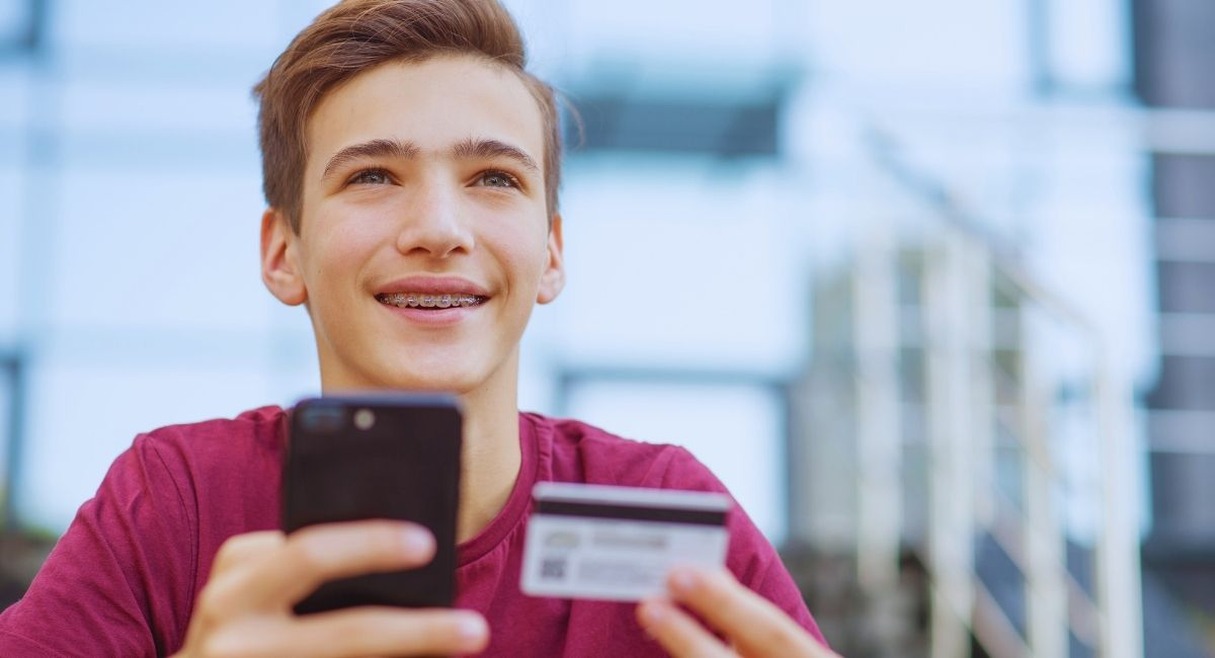Adolescent souriant tenant une carte bancaire et un smartphone pour payer en ligne